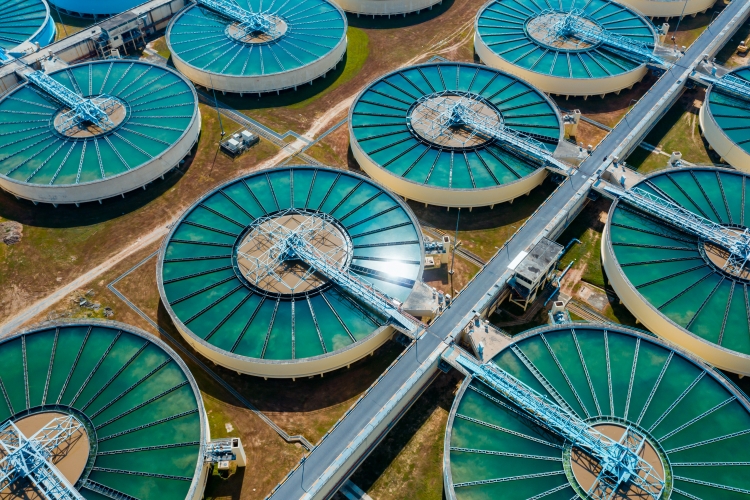 Foto: Luftaufnahme von einem Wasserwerk bei Sonnenschein. Zu sehen ist eine Reihe von türkisfarben schimmernden Nachklärbecken.