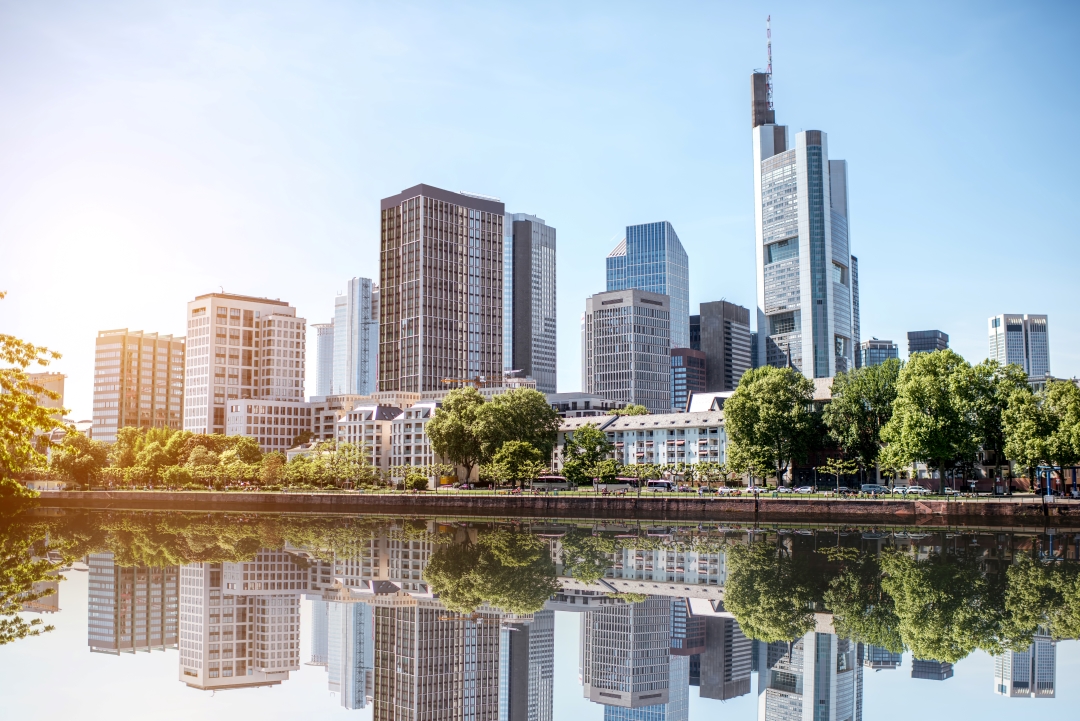 Foto: Panorama der Frankfurter Skyline. Es sind Hochhäuser im Sonnenschein zu sehen.