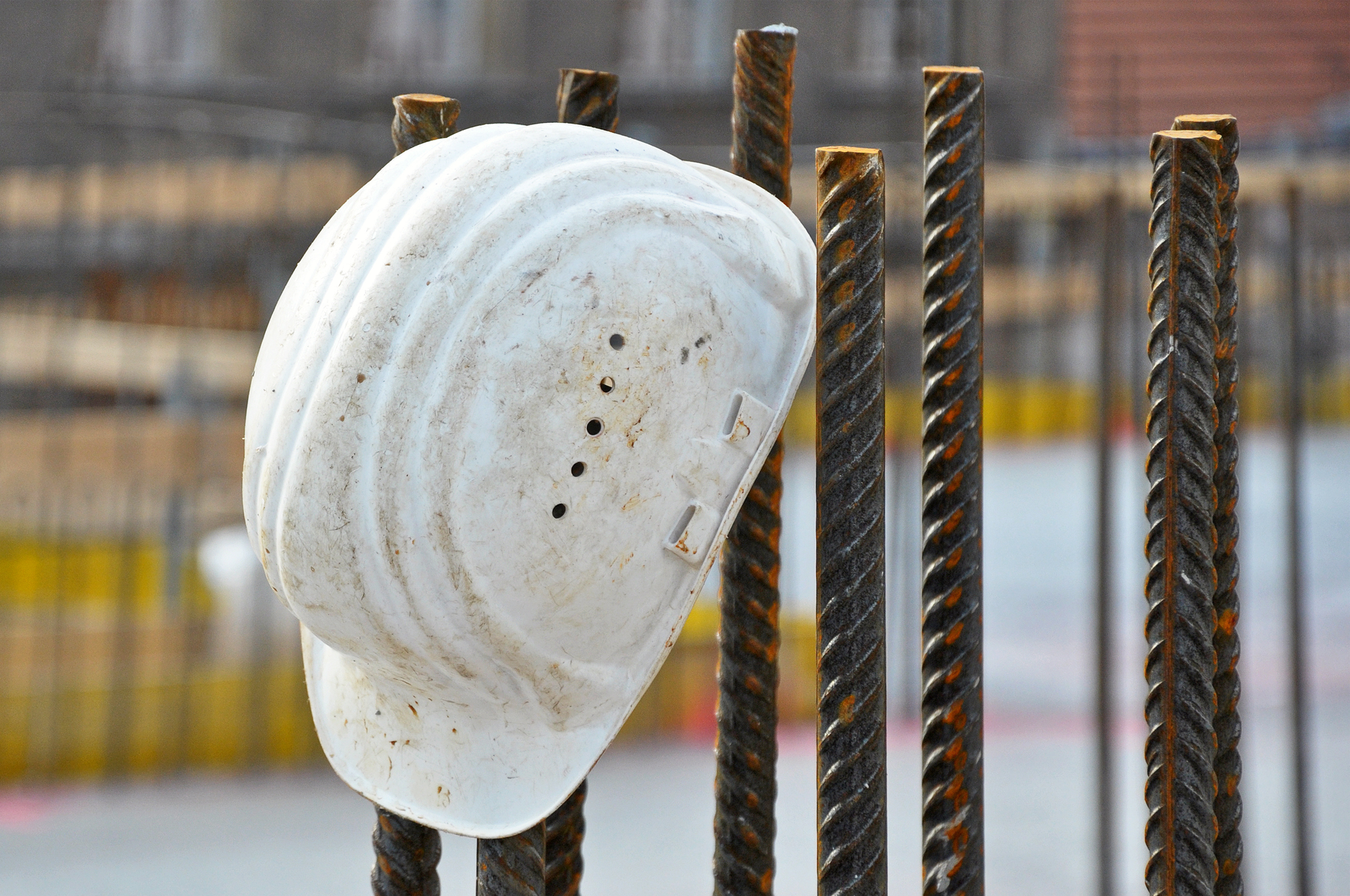 Foto: Ein weißer Schalenhelm hängt auf einer Baustelle auf einer Stahlstange.