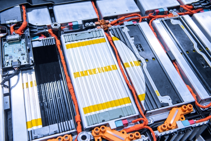 Foto: Das Batteriemodul eines Elektrofahrzeugs. Die Hülle besteht aus hellem Aluminium, dazwischen liegen orangefarbene Kabel und Klemmen.