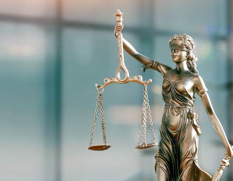 Photo: A brass statue of Justice against a blurred, light blue background.