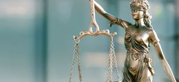 Photo: A brass statue of Justice against a blurred, light blue background.