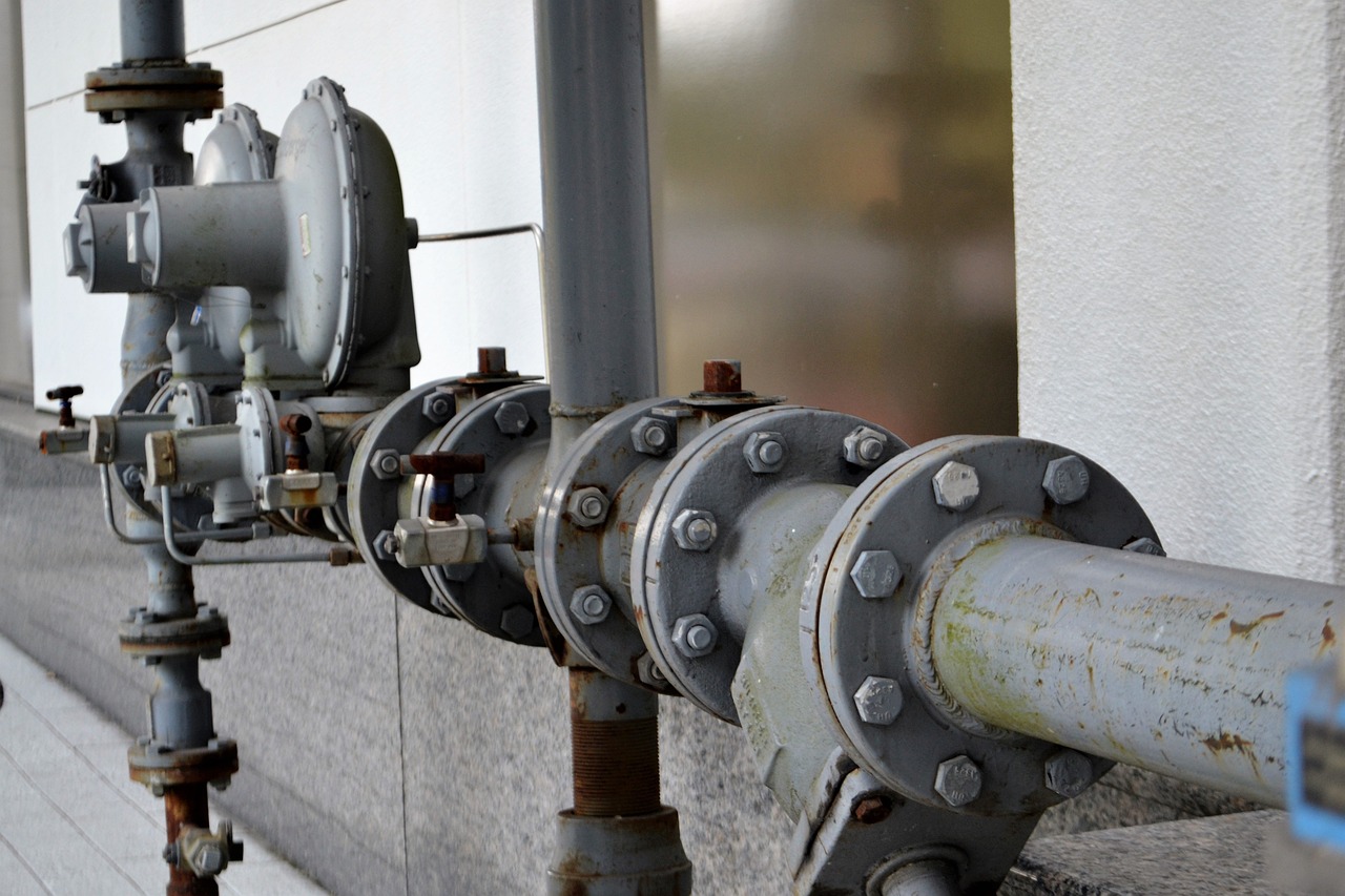 Foto: Eine industrielle Wasser- oder Gasleitung mit mehreren Ventilen und Rohren, die entlang einer Gebäudewand verlaufen.